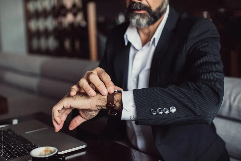 Beared businessman on suit with laptop and coffee looking his watch