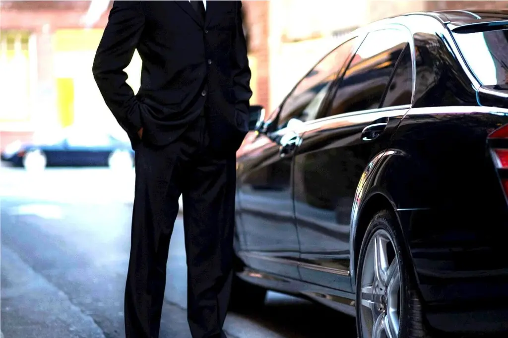 Private chauffeur in black suit waiting full time service transfer next to black Mercedes-Benz