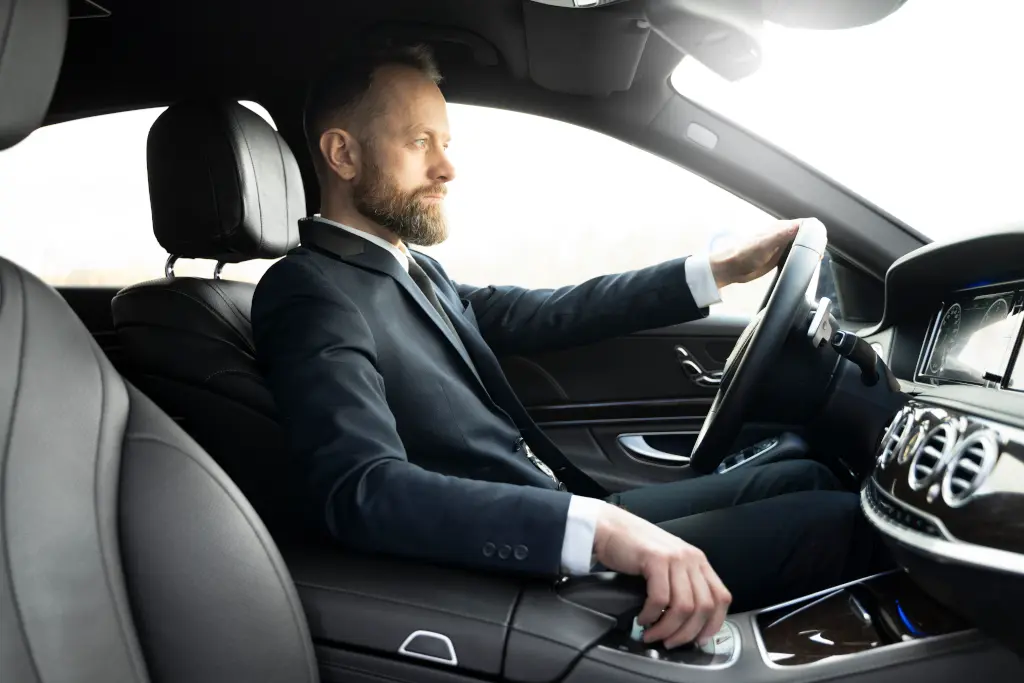 Side view young elegant bearded man driving luxury car transfer service